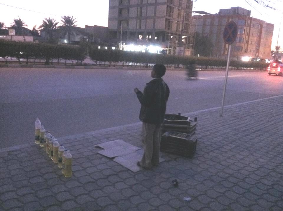 صورة لطفل يبيع البانزين ويؤدي صلاة المغرب على الرصيف وسط كربلاء