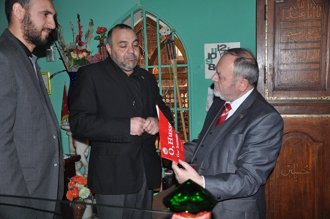 السفير الروماني يستلم راية حمراء مكتوب عليها (ياحسين) ويقول انه :يؤدي الصلوات ويصوم في رمضان(مصور)